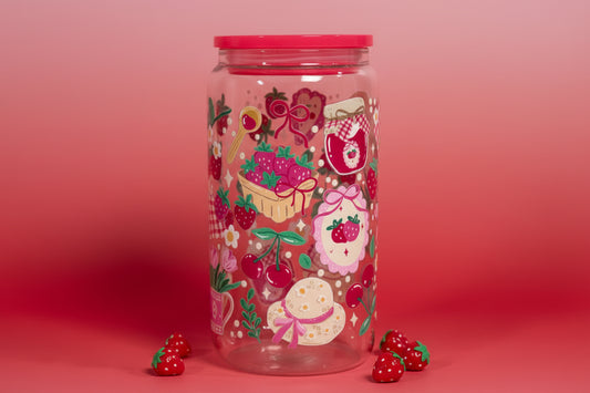 Clear tumbler with colorful strawberry-themed design and red lid on a marble surface.